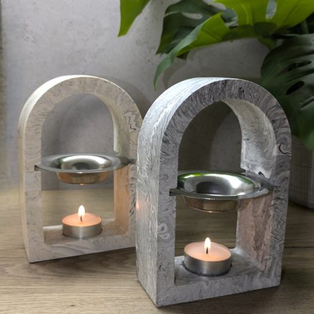 A pair of wax melt burners, arched design with metal dish. Resting on a Wooden surface, green leaves and grey in the background.