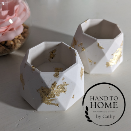 Pair of white Tea light holdes with gold fleck design, sat on a white background with a pink flower in the background.