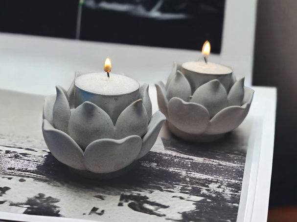 Pair of Lotus Flower Shaped Tea Light Holders, resting on a white and grey surface. The candles are lit.